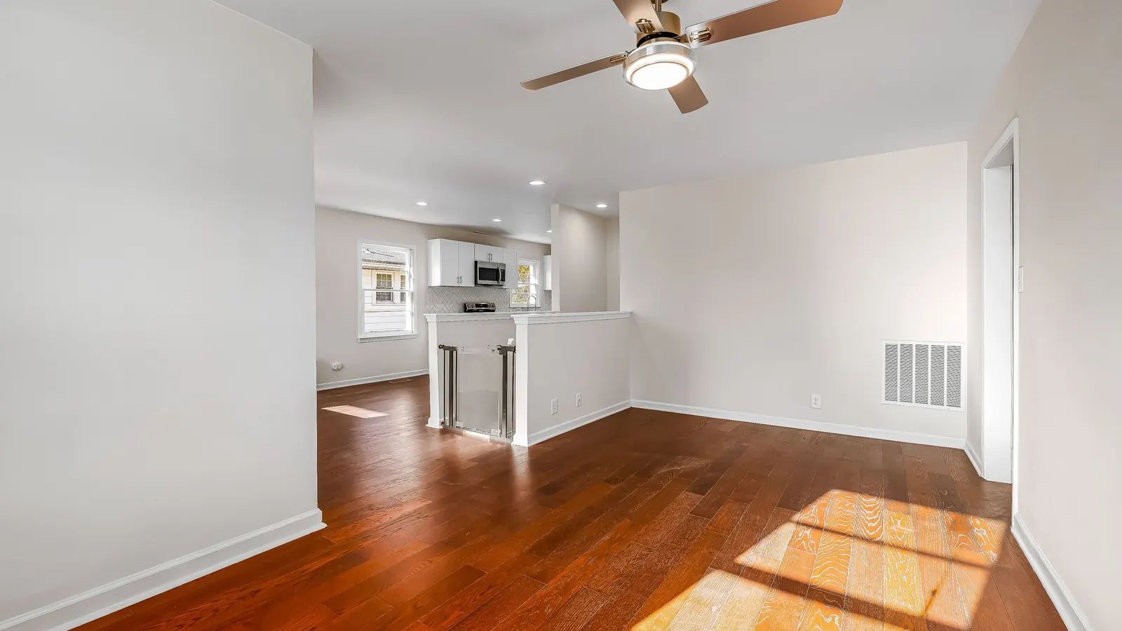 Vacant apartment unit with wood floors, ceiling fan and open kitchen between tenants