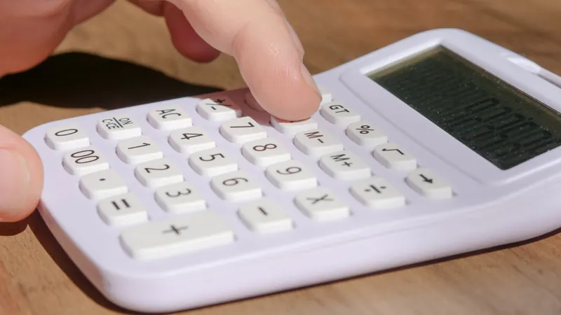 Finger pressing keys on a white desk calculator, working out what a house cleaning price covers
