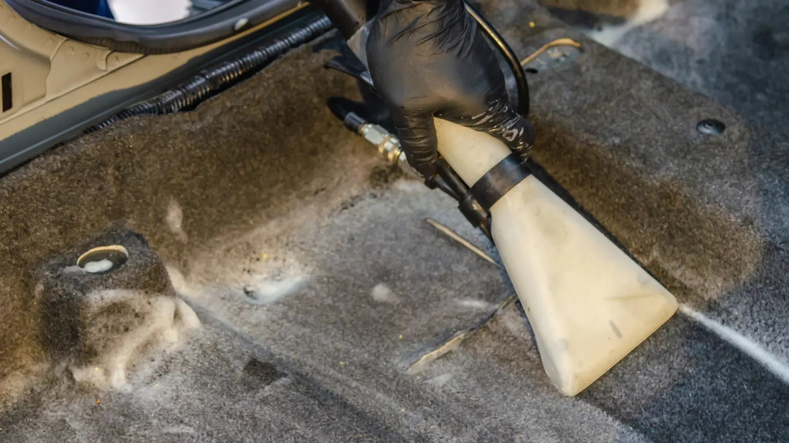 Gloved hand pulling an extraction tool across dirty carpet fibers