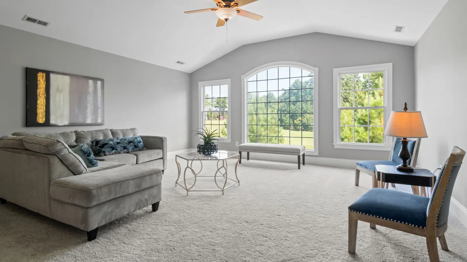 Bright living room with wall-to-wall beige carpet, gray sectional sofa and arched windows