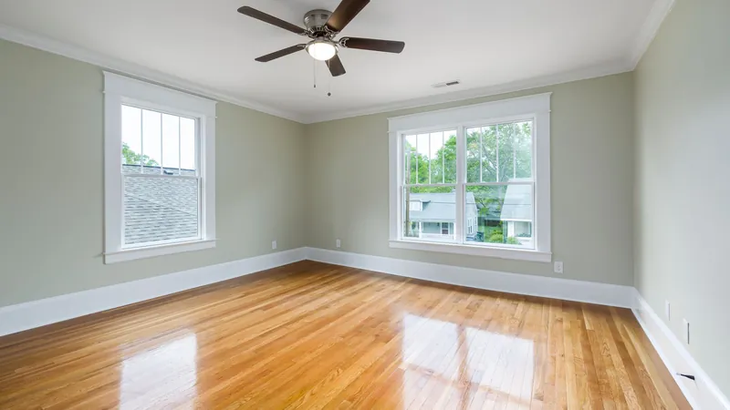 Empty living room with wood floors, large windows and a ceiling fan