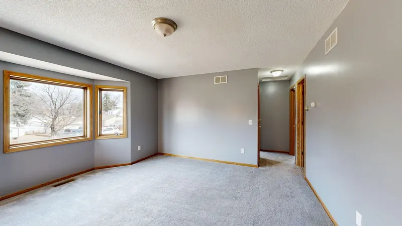Empty apartment living room with light gray wall-to-wall carpet and a bay window