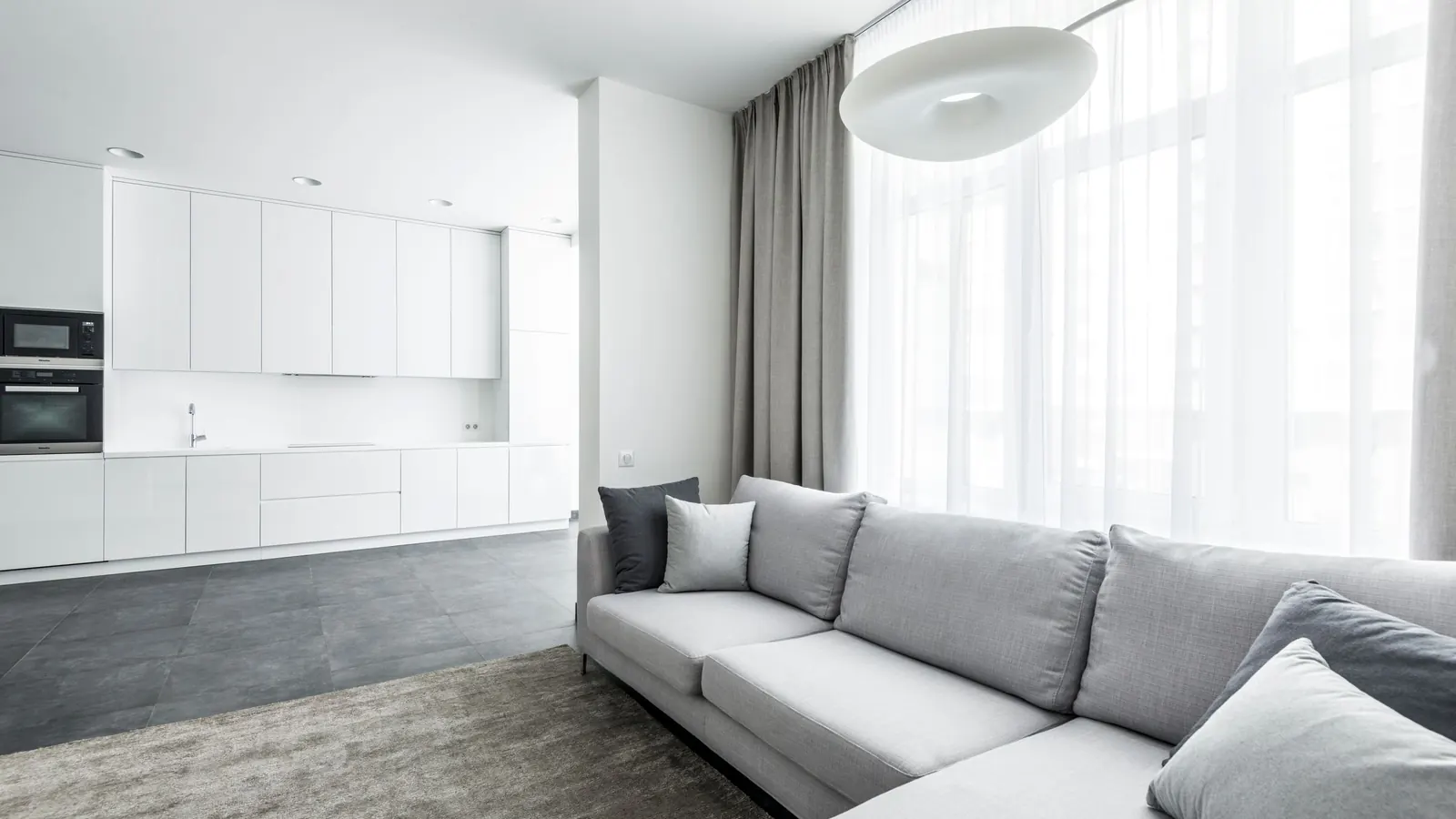 Light gray fabric sectional sofa in a bright open-plan living room with a white kitchen