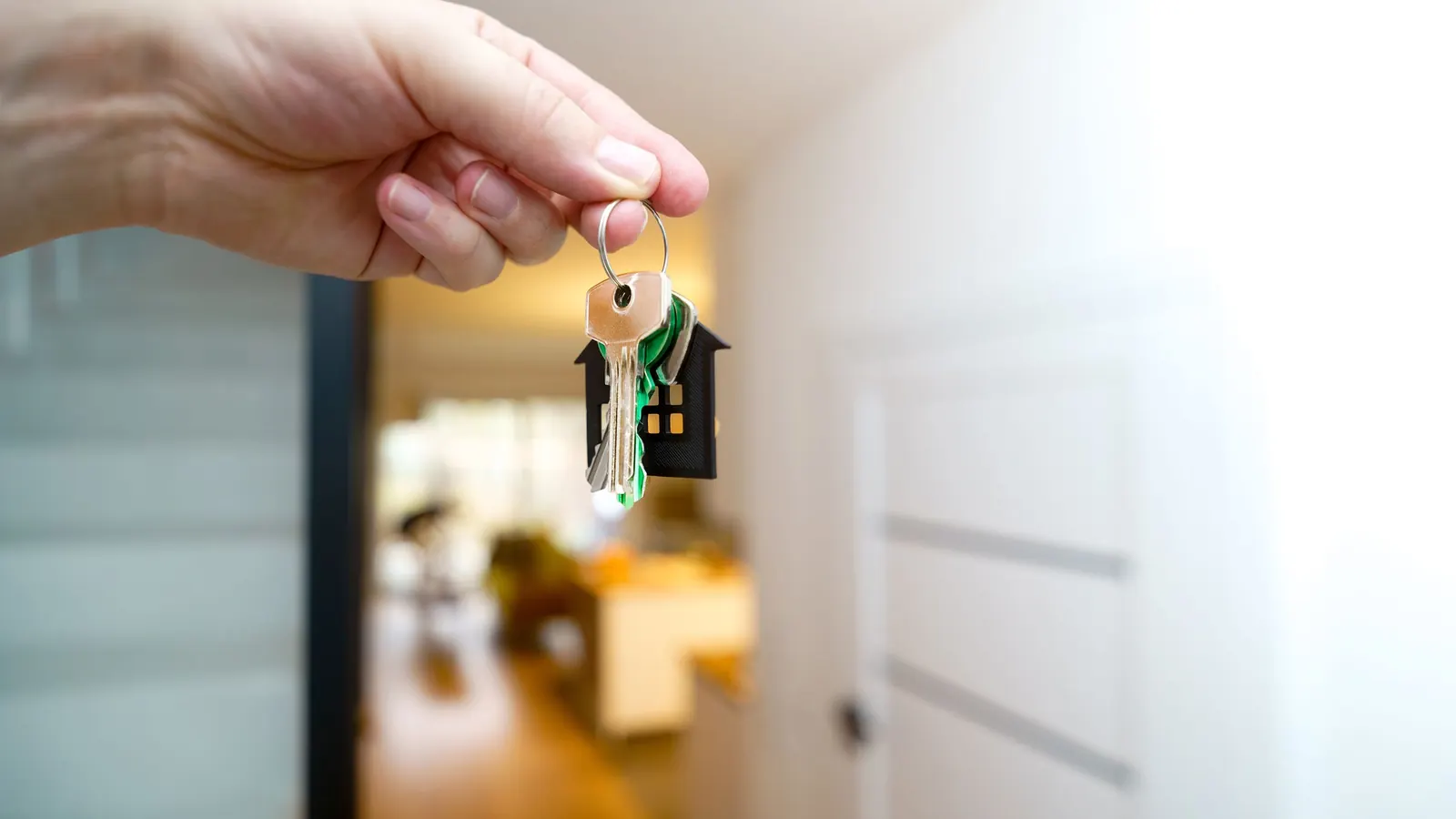Hand holding a set of house keys on a house-shaped keychain inside an apartment entry