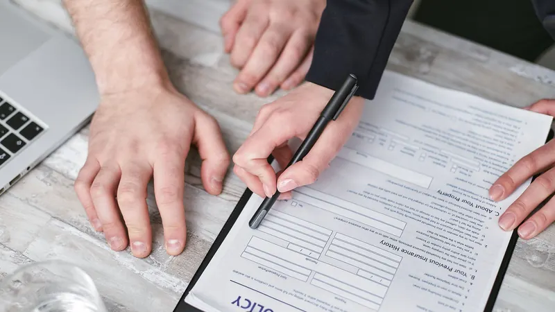 Hands pointing to an insurance policy form on a clipboard with a pen