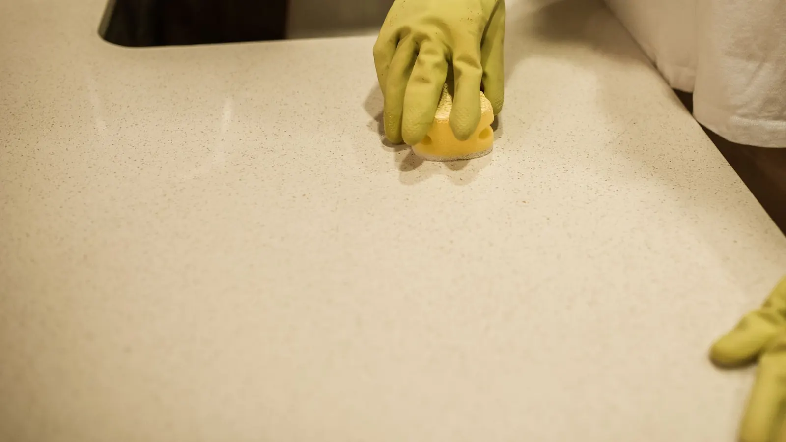 Hand in a yellow rubber glove wiping a speckled white kitchen counter