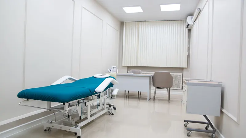 Clean medical exam room with a teal treatment table, white walls and polished floor