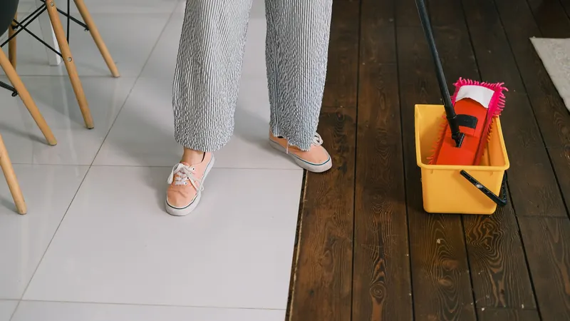 Mop in a yellow bucket on a wood floor next to white tile, as in a shared building hallway