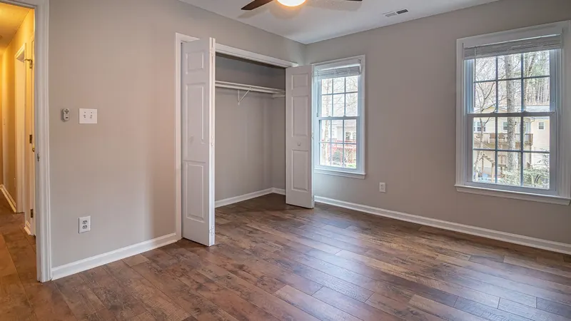Empty bedroom with dark wood floors, open closet doors and a ceiling fan, ready for move-out