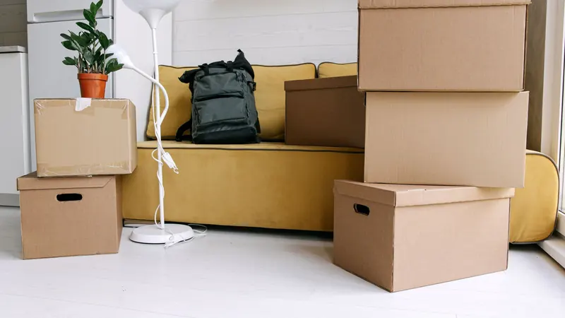 Stacked cardboard moving boxes in front of a yellow sofa in a bright apartment