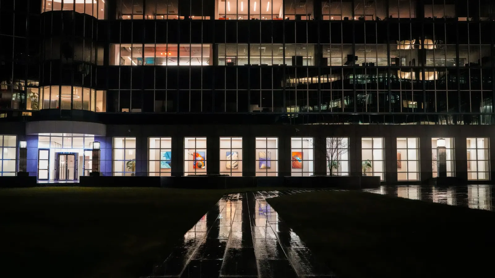 Office building at night with lit floors and an empty lawn in front
