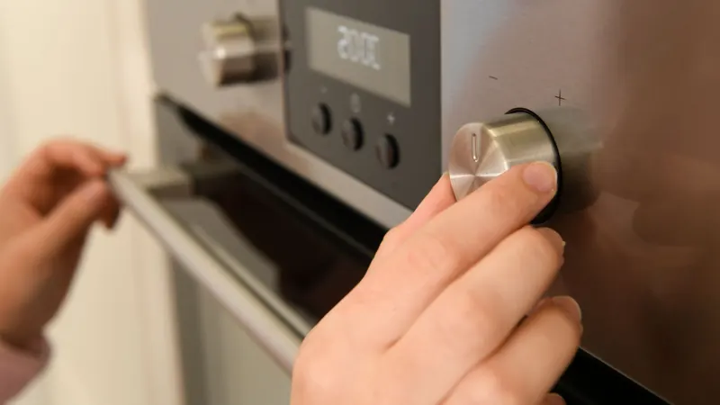 Hand opening a stainless steel wall oven door next to the control knob