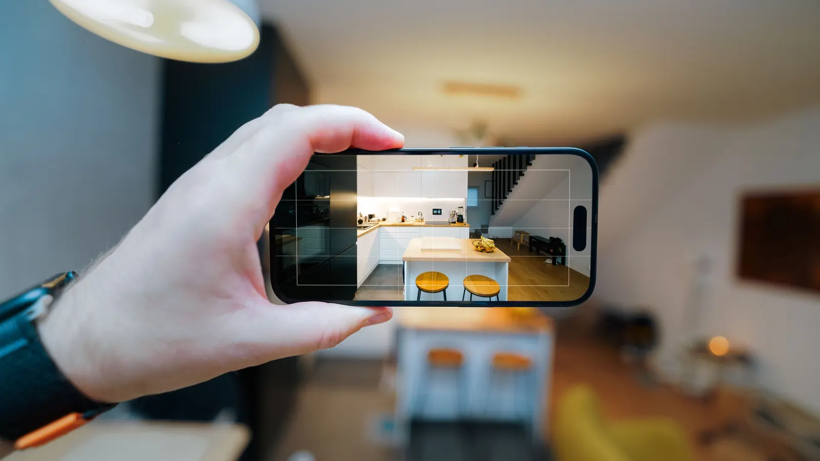 Hand holding a phone to photograph a kitchen and dining area, as when sending photos to a new cleaner