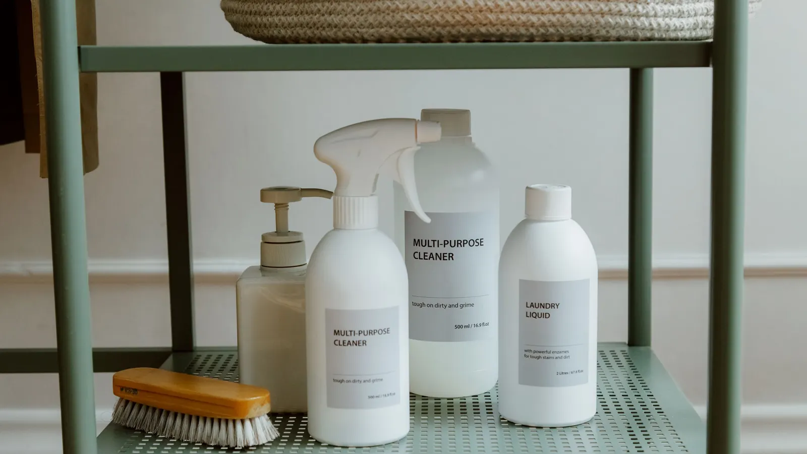 Unbranded refillable cleaner bottles and a scrub brush on a green metal shelf