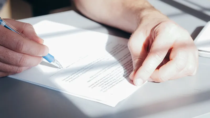 Hand signing a printed contract with a blue pen, as when an office changes cleaning vendors