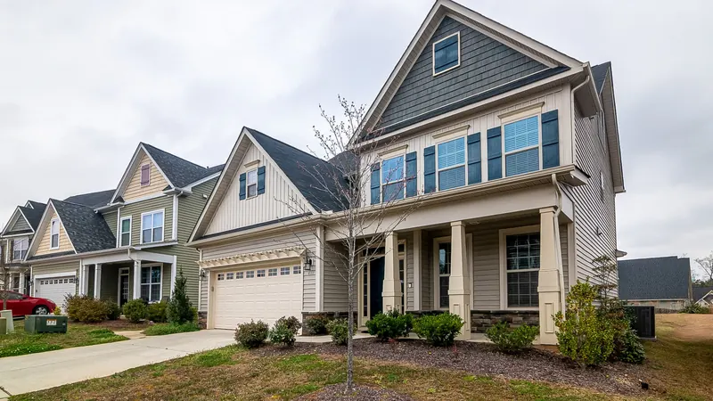 Two-story suburban house with gray siding, front porch and lawn under an overcast sky