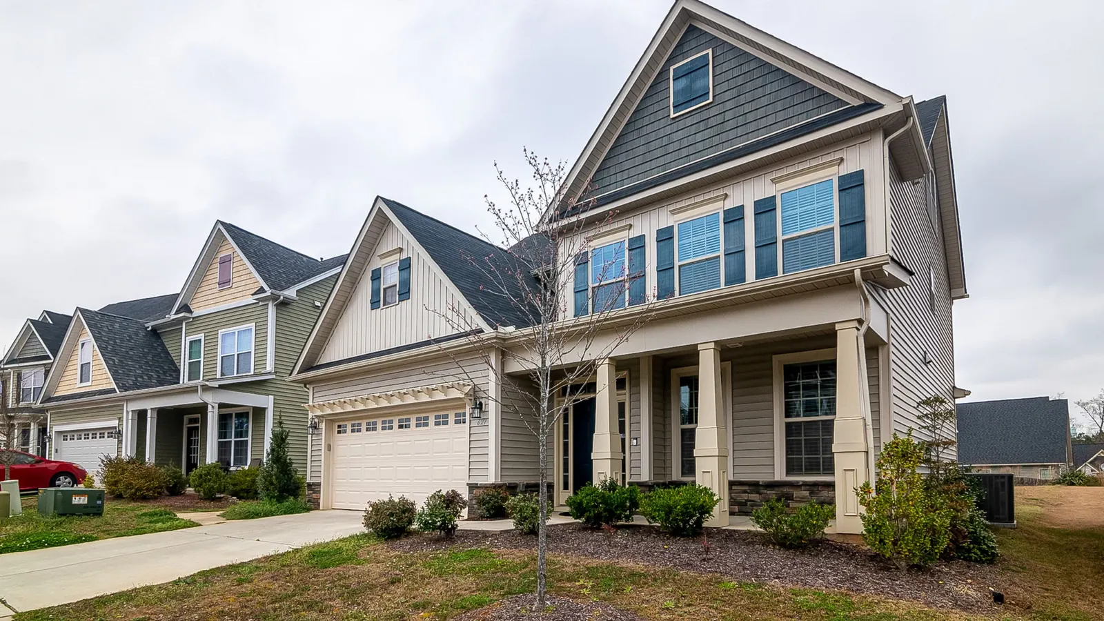 Two-story suburban house with gray siding, front porch and lawn under an overcast sky