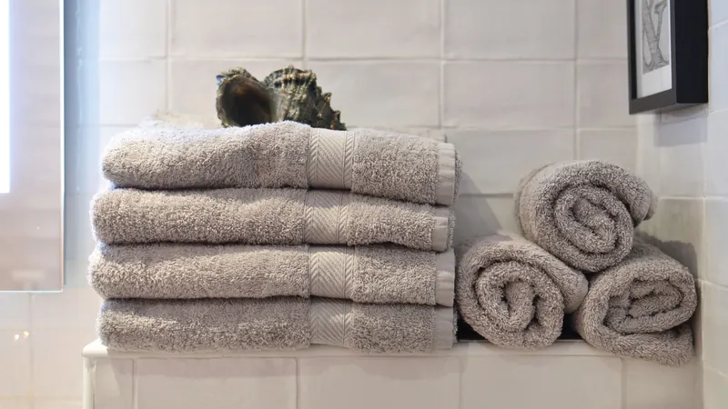 Stack of folded gray bath towels and rolled hand towels on a white tiled bathroom shelf