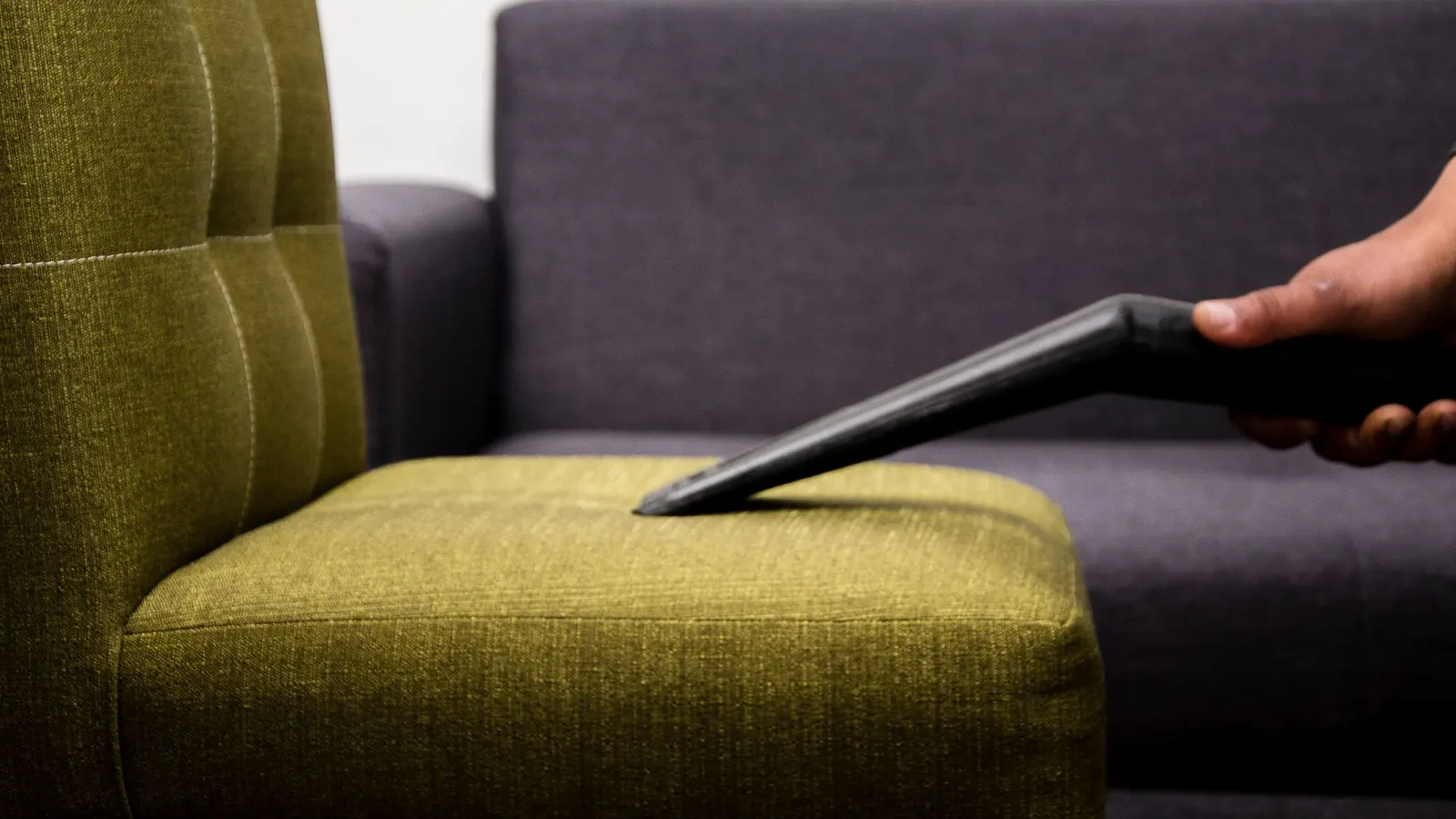 Upholstery cleaning tool pressed against a green fabric chair seat next to a gray sofa