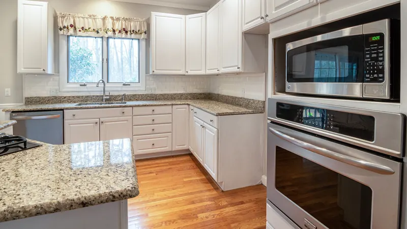 Stainless steel wall oven and microwave in a kitchen with white cabinets and granite counters