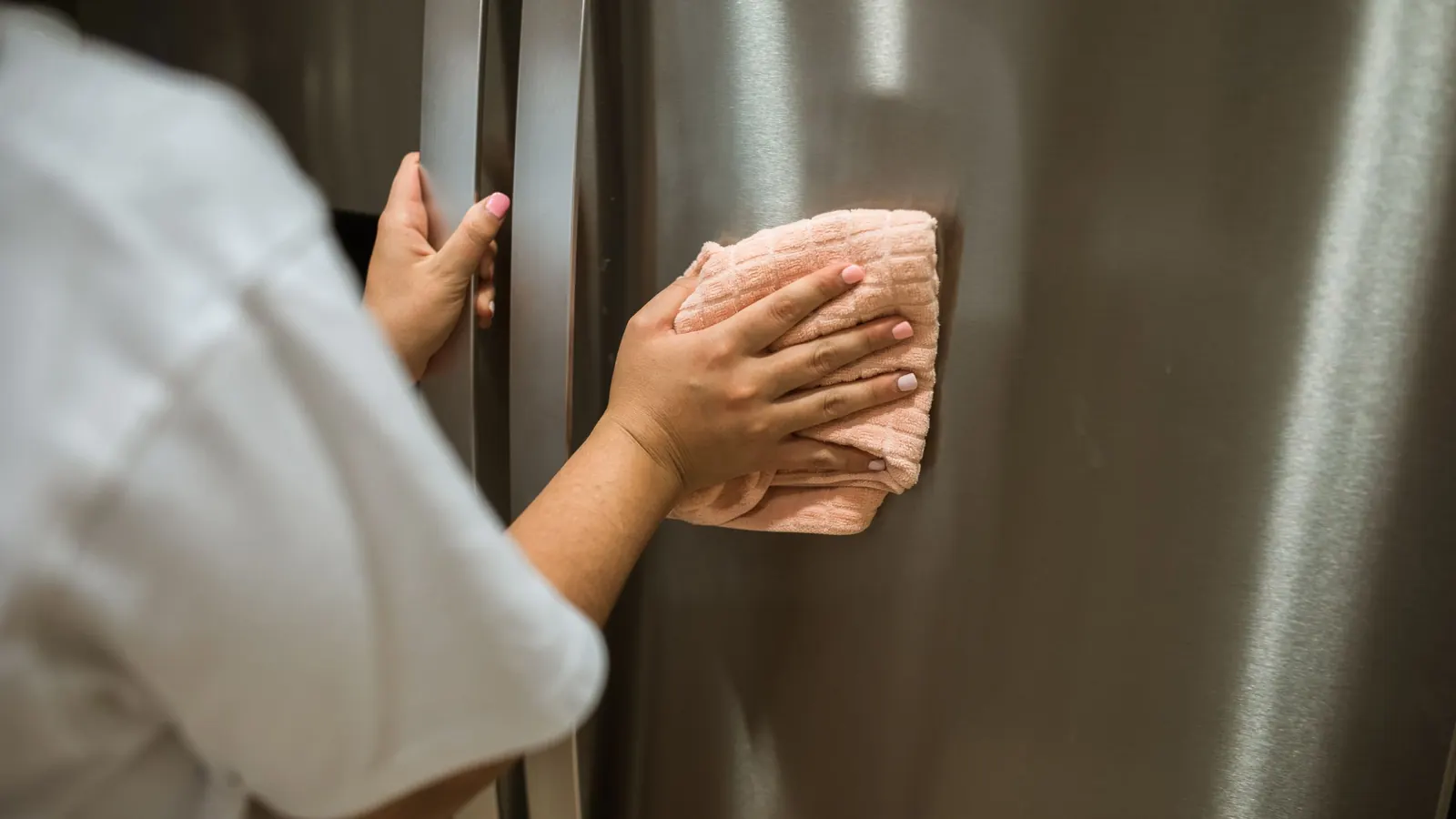 Hand wiping a stainless steel refrigerator door with a soft cloth during a house cleaning