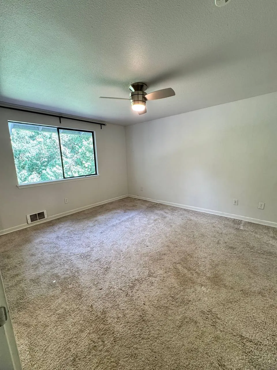 Before: bedroom carpet under a ceiling fan and wide window