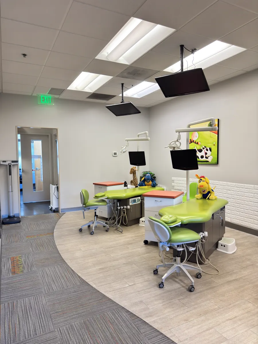 Pediatric dental clinic, two open treatment bays with green chairs and clean floors