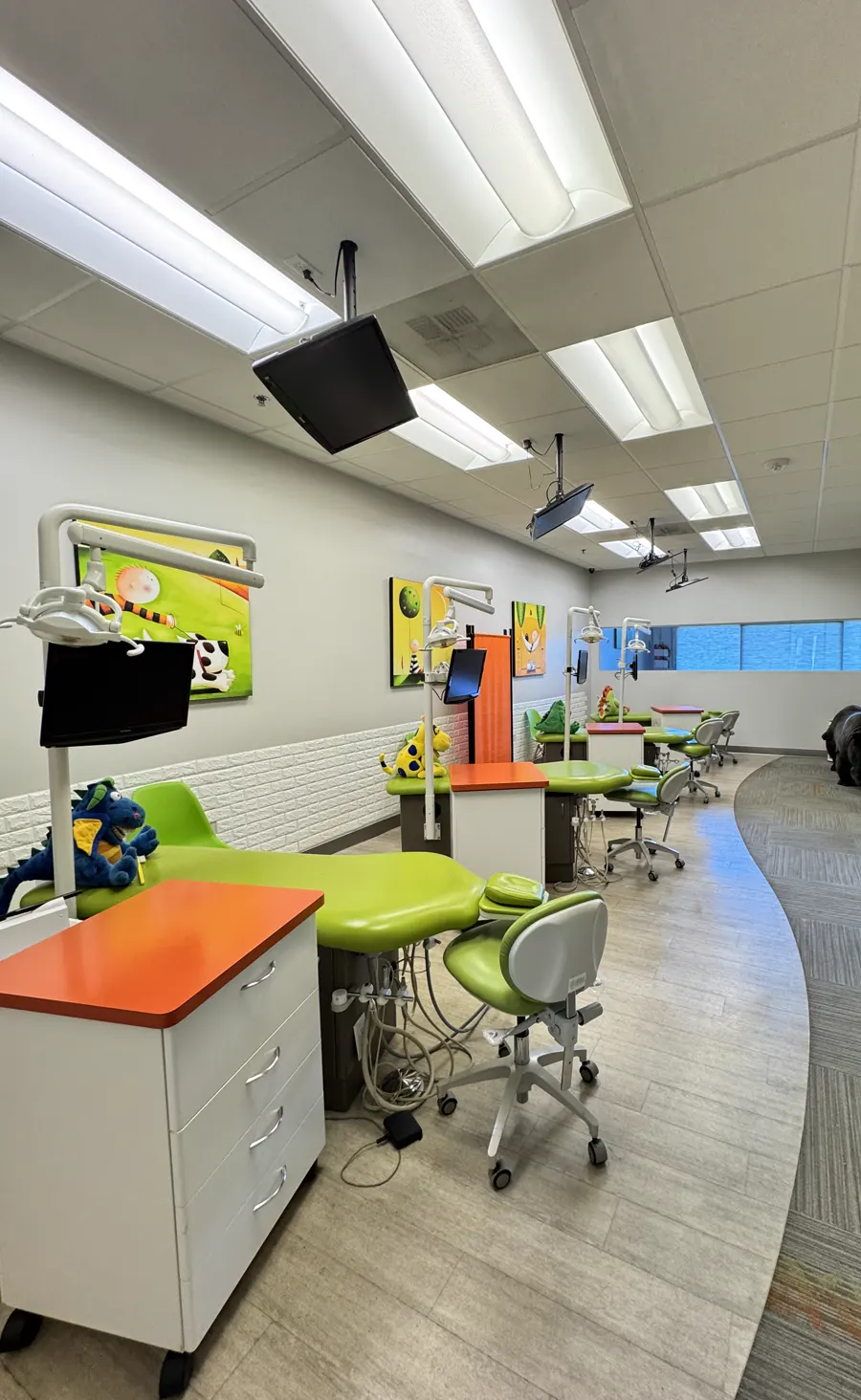 Row of pediatric dental chairs along a wall, clean vinyl floor and carpet path