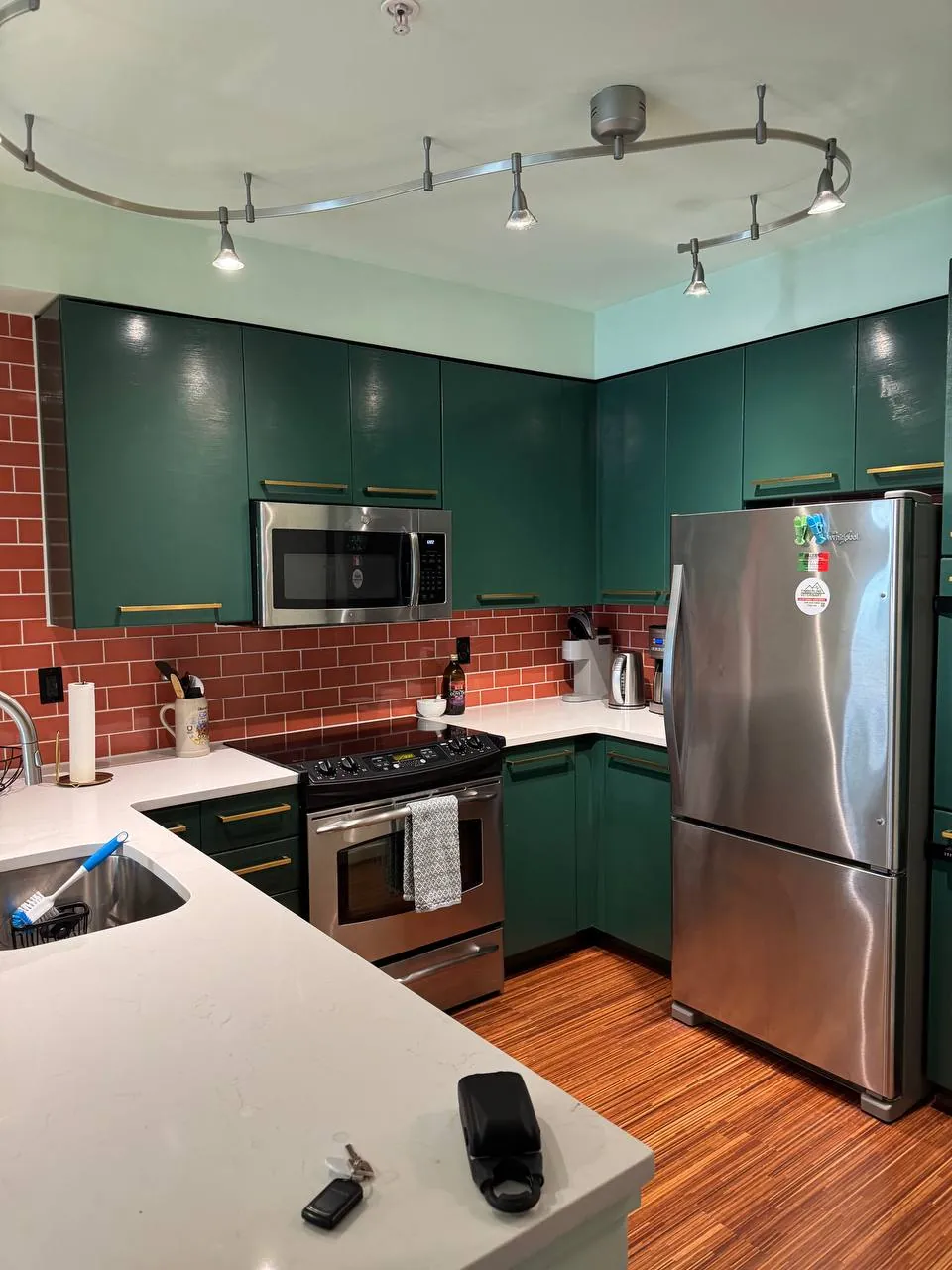 Before: kitchen with green cabinets, counters and stainless fridge
