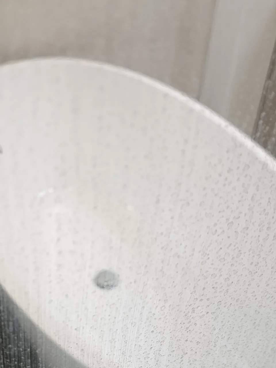 Before: freestanding tub seen through a glass shower panel, hard-water spots on the glass before