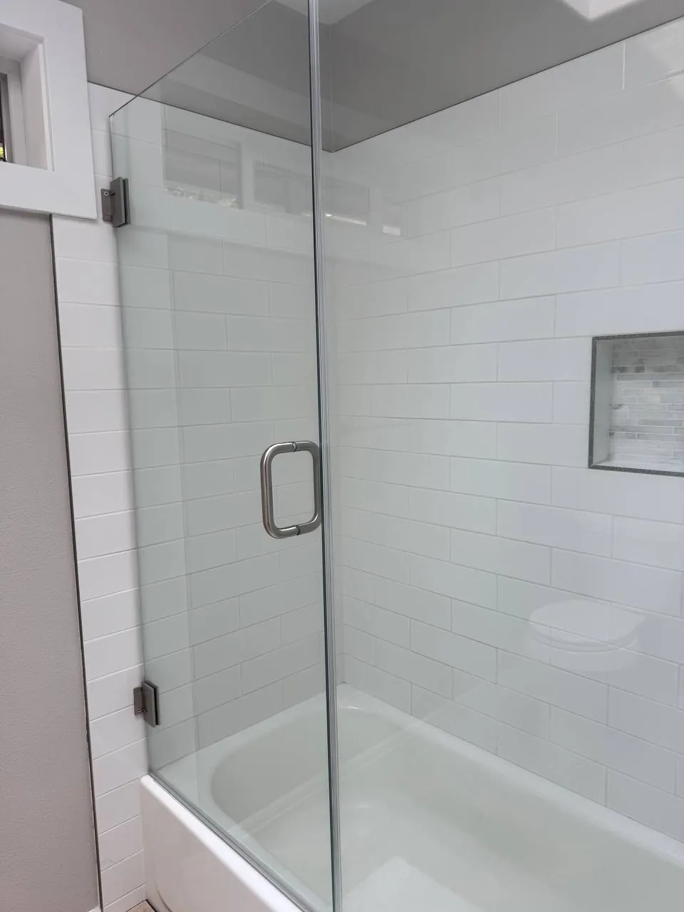 Glass shower panel over a tub with white subway tile