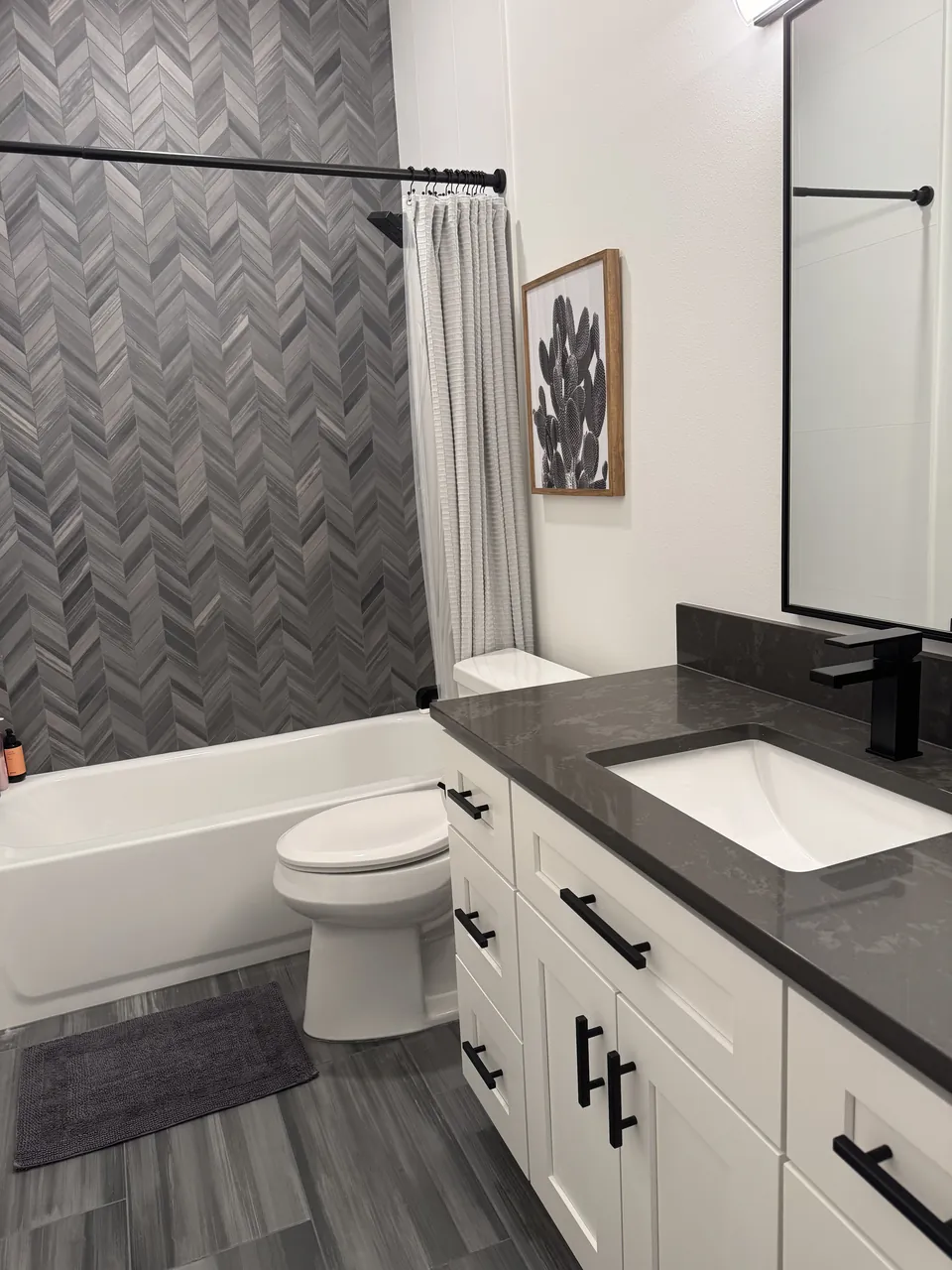 Bathroom with white vanity, dark counter, toilet and herringbone tile wall