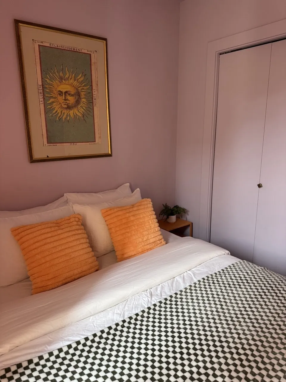 Made bed with orange pillows and a checkered throw in a pink bedroom