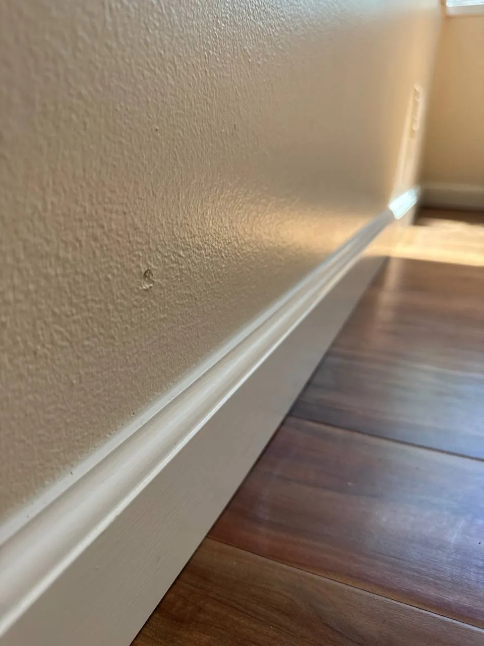 Close-up of a white baseboard along a hardwood floor