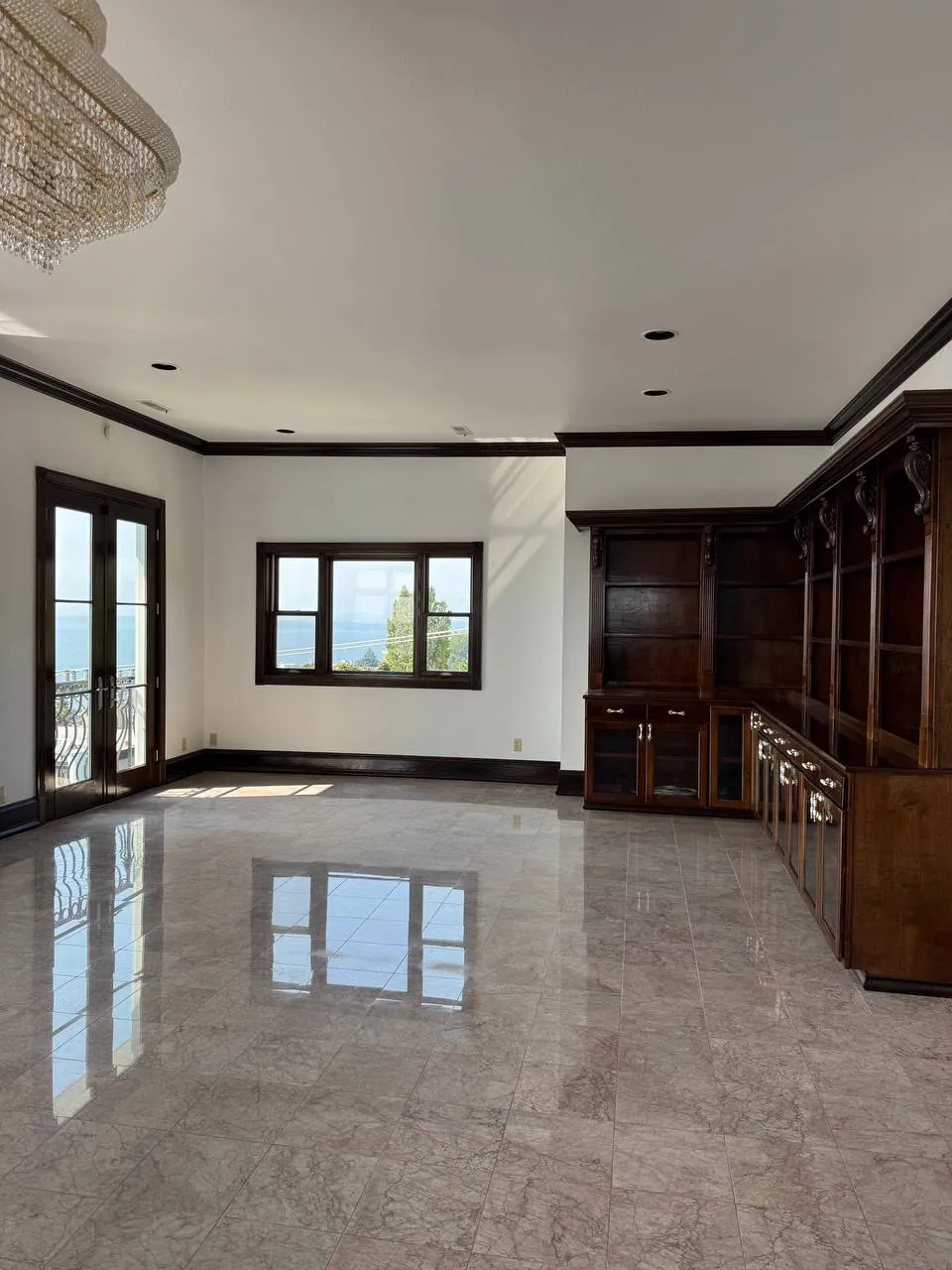 Finished living room with polished stone floor, chandelier and built-in dark wood cabinets