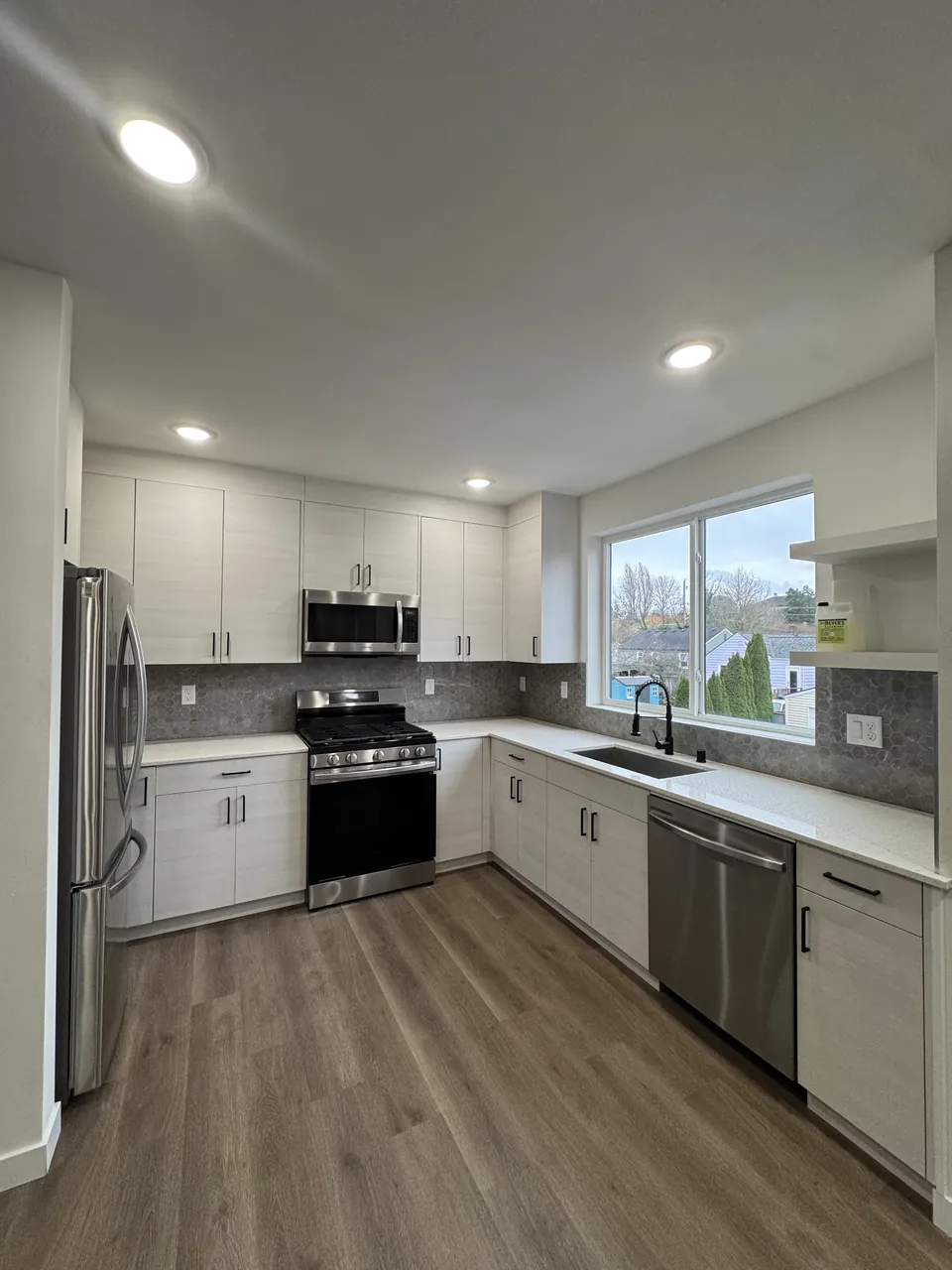 Empty kitchen with white cabinets, stainless appliances and vinyl plank floor