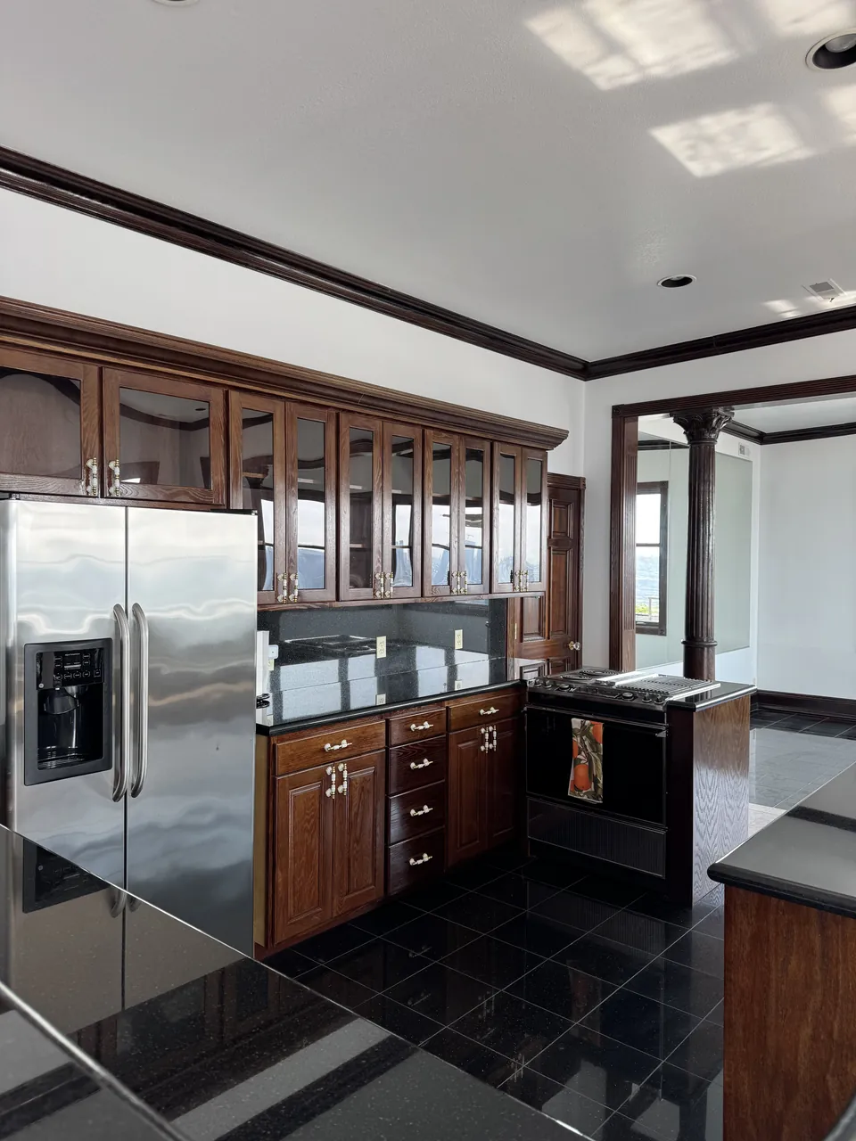 Finished kitchen with dark wood glass-front cabinets, stainless fridge and black tile floor