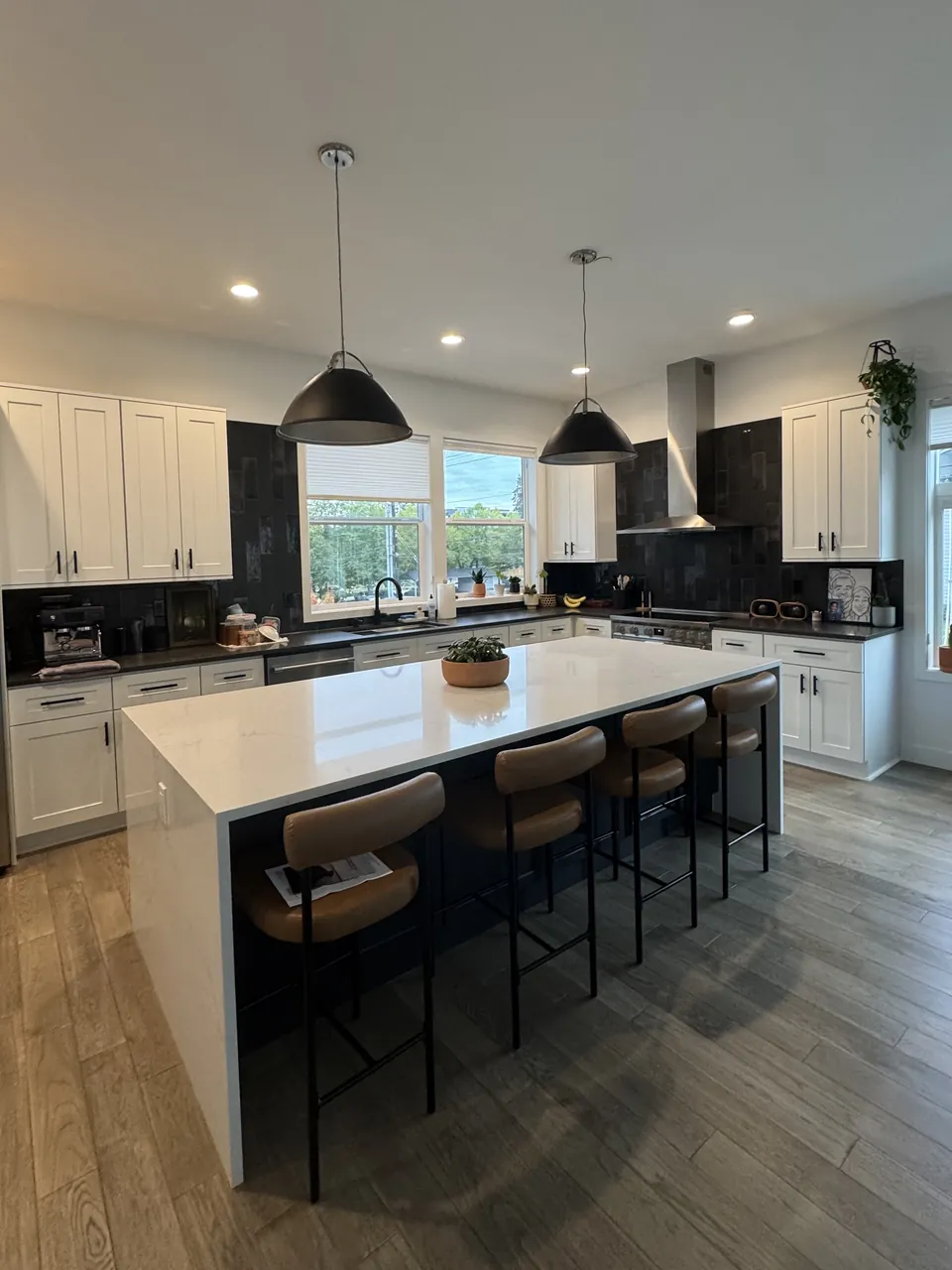 Bright kitchen with white and black cabinets, waterfall island, stools and pendant lights